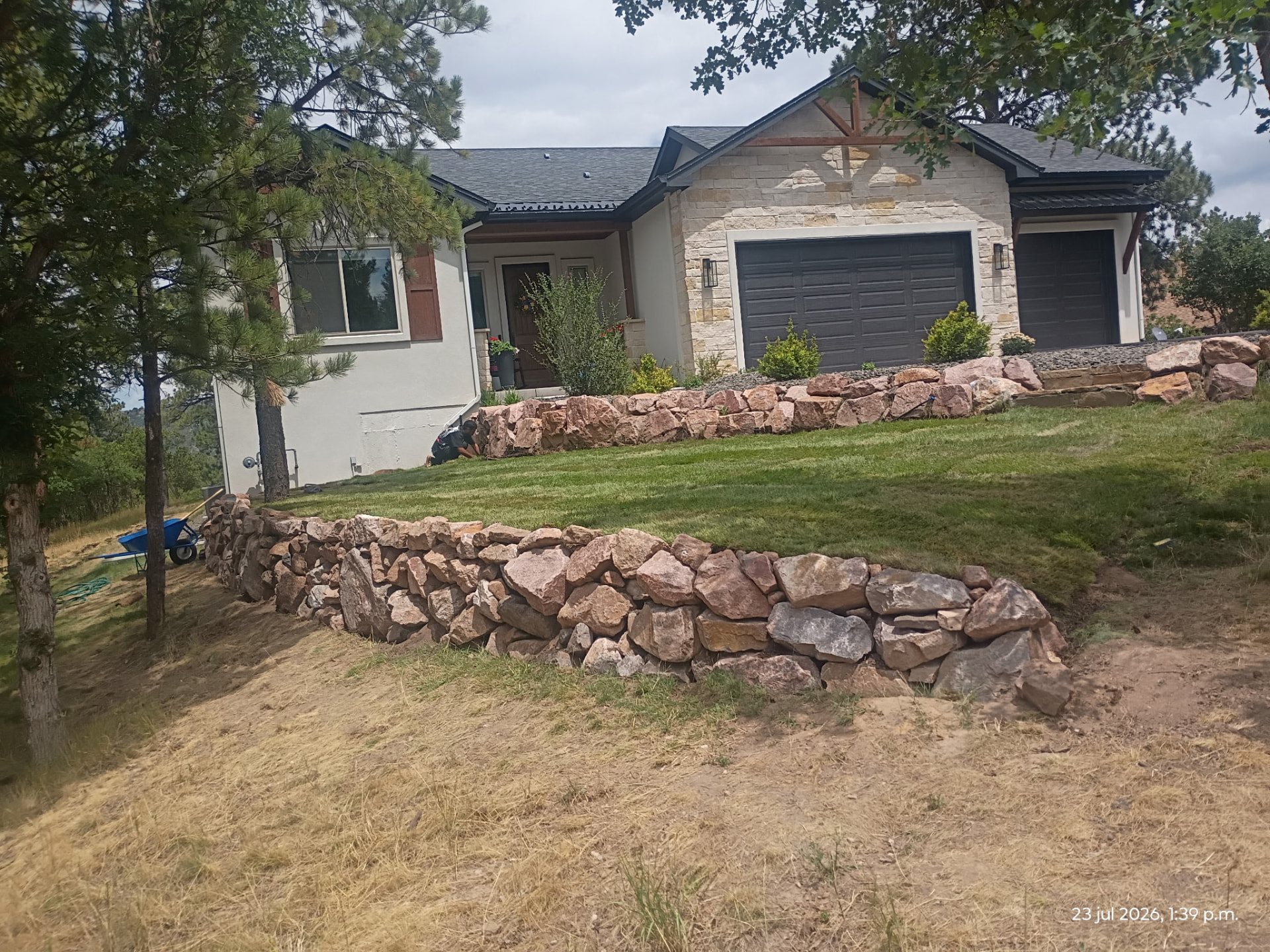 Terraced boulder retaining walls with a fresh sod lawn below a stone-front Colorado home